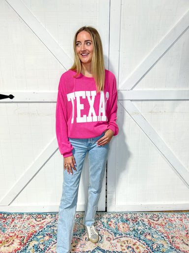 Photo of a woman modeling our magenta Texas sweatshirt with large white bold letters saying TEXAS across the front