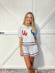 Woman modeling a grey cotton shorts set with red, white and blue sequins trim around sleeves, bottom of shirt and bottom of shorts saying USA in red, white and blue yarn