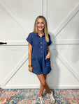 Woman wearing our navy short sleeve romper that has a collar, buttons up and has pockets