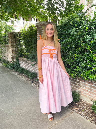 A girl modeling our light pink with orange spaghetti straps and in two stripes at the bodice of the dress. The bodice is also shirred and then has a straight midi skirt