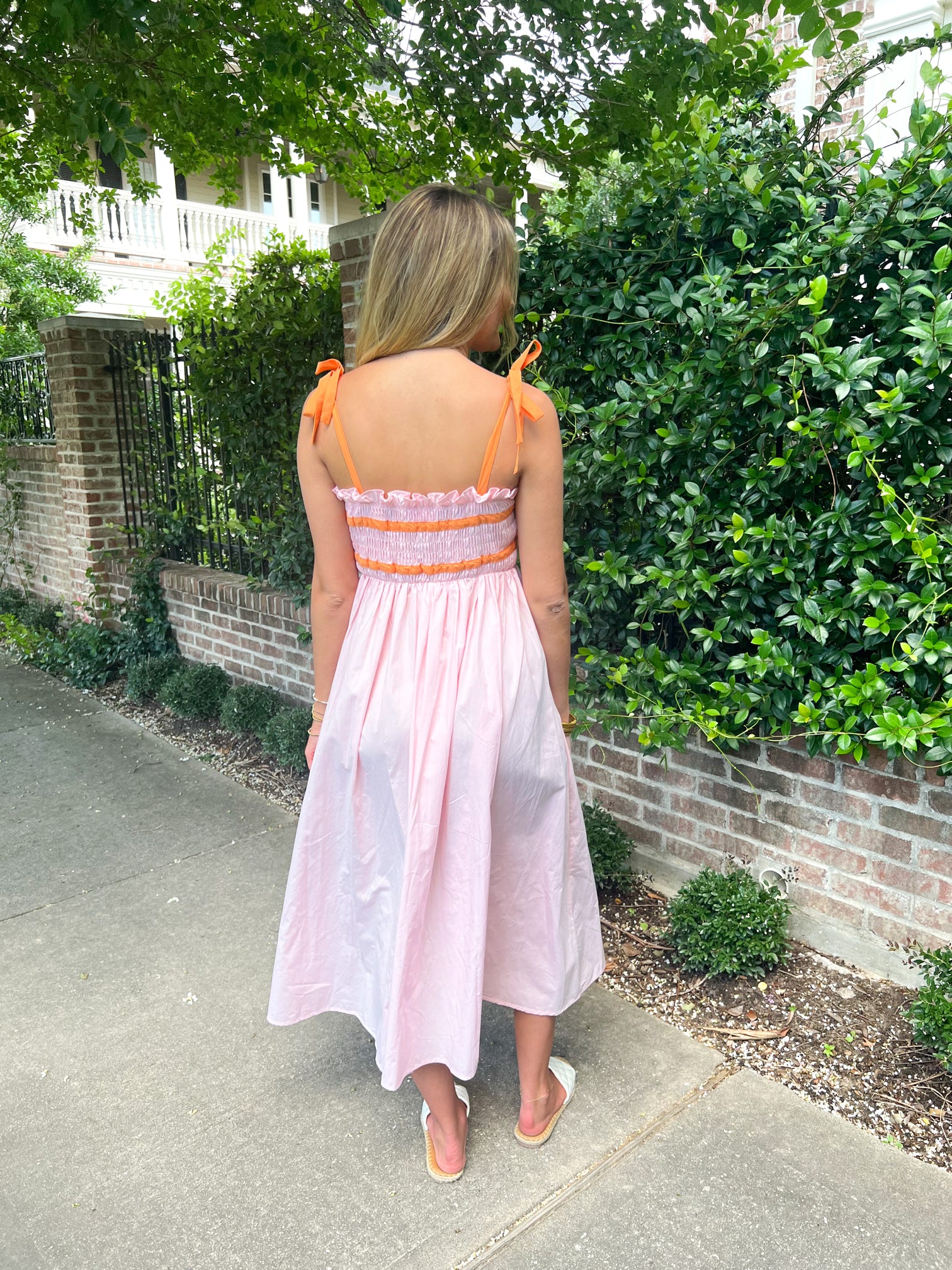 A girl modeling the back of our light pink with orange spaghetti straps and in two stripes at the bodice of the dress. The bodice is also shirred and then has a straight midi skirt