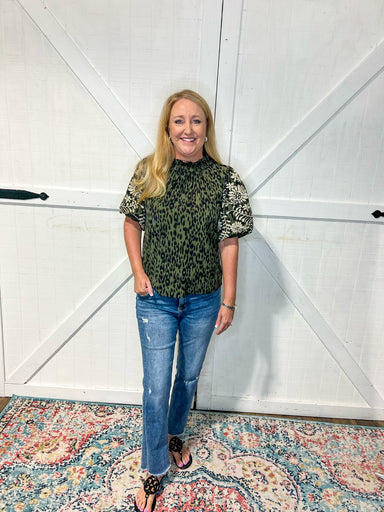 Photo of a woman modeling a dark green top featuring a cheetah pattern and playful cream floral embroidery on the sleeves