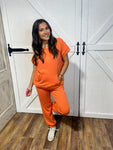 Photo of a young woman wearing our orange, short sleeve top with pocket and matching sweatpants. Lightweight and comfy!