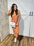 Photo of a woman modeling the front of our clay colored sleeveless maxi cotton dress. She is holding our white Jon Hart Crossbody Purse and wearing fun sneakers.