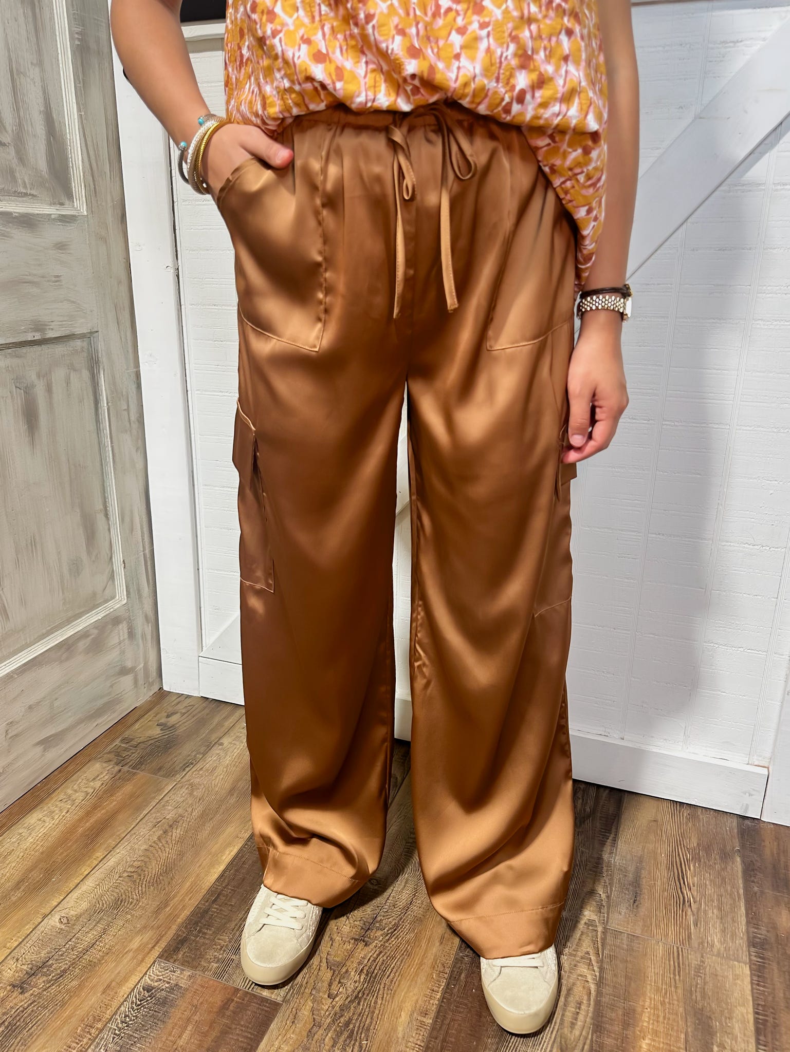 Up close photo of a young woman modeling our camel colored satin feeling cargo pants with pockets on the side.