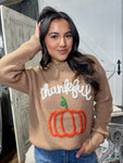 Up close photo of our brown sweater with Thankful and a pumpkin stitched in yarn on the front