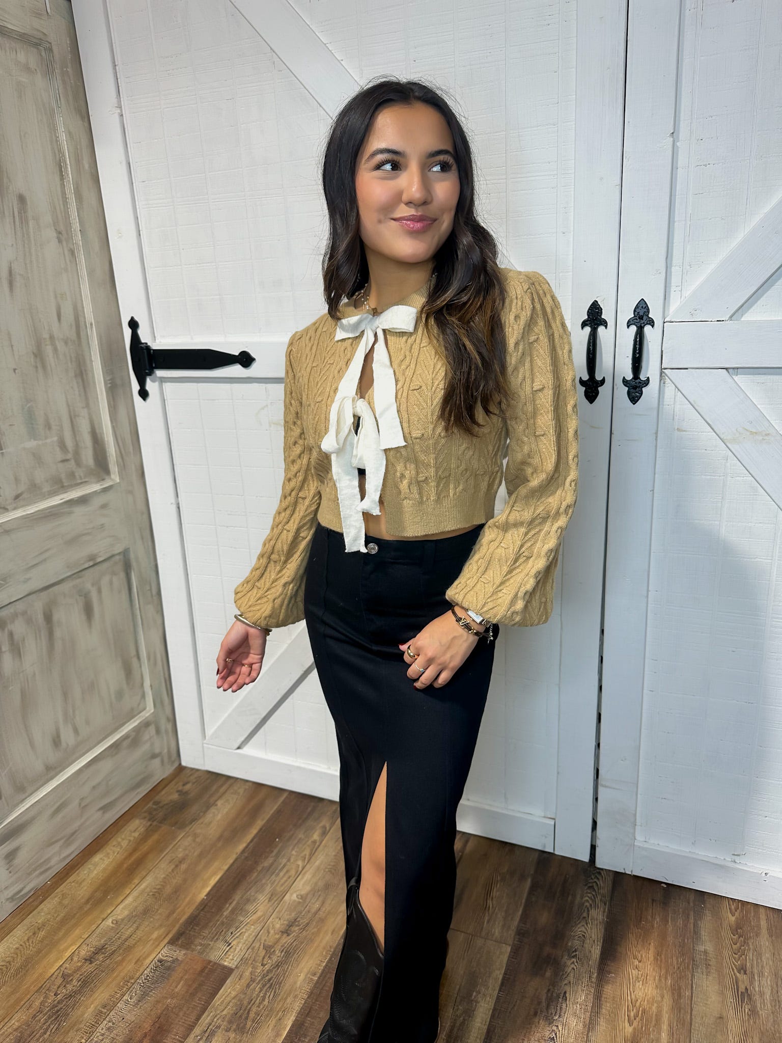 Young woman modeling our tan, long sleeve cardigan sweater with bow ties where buttons would be. 