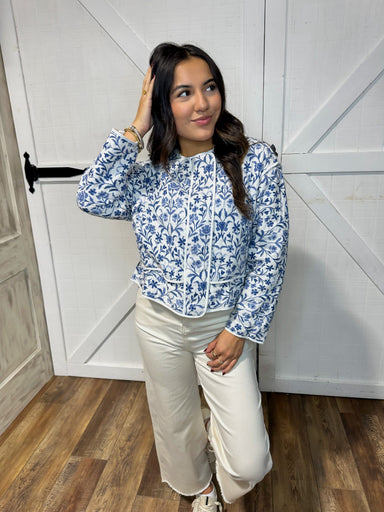 Woman modeling  our white quilted jacket with a blue floral pattern all over