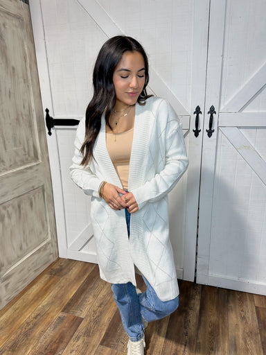 Woman modeling our white long cardigan with gold stitching in an X pattern all over