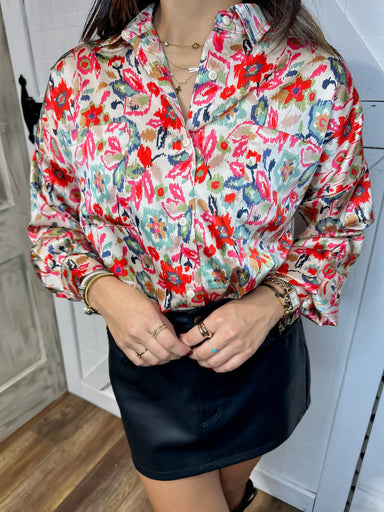 Up close photo showing the  beige button down blouse with a vibrant pattern of red, navy, green, and pink leaves and flowers 