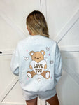 Young woman modeling the back of the sweatshirt with the same teddy bear holding the love you heart embroidered big. It comes with matching grey shorts (not embroidered).