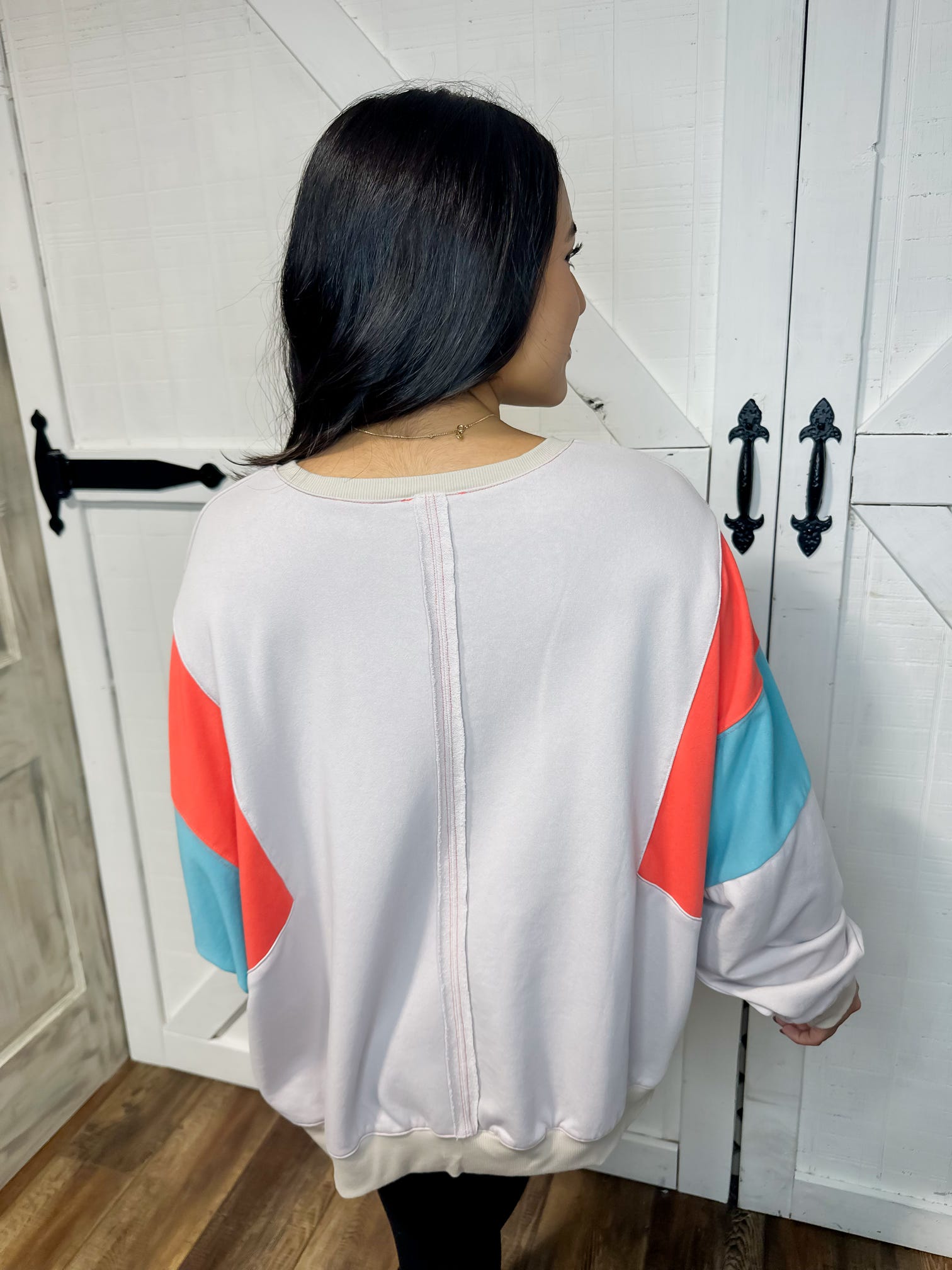 Photo of the back of our beige lightweight sweatshirt featuring a bold orange and turquoise stripe on the arms.