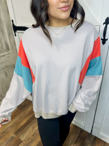 Up close photo of our beige lightweight sweatshirt featuring a bold orange and turquoise stripe on the arms.