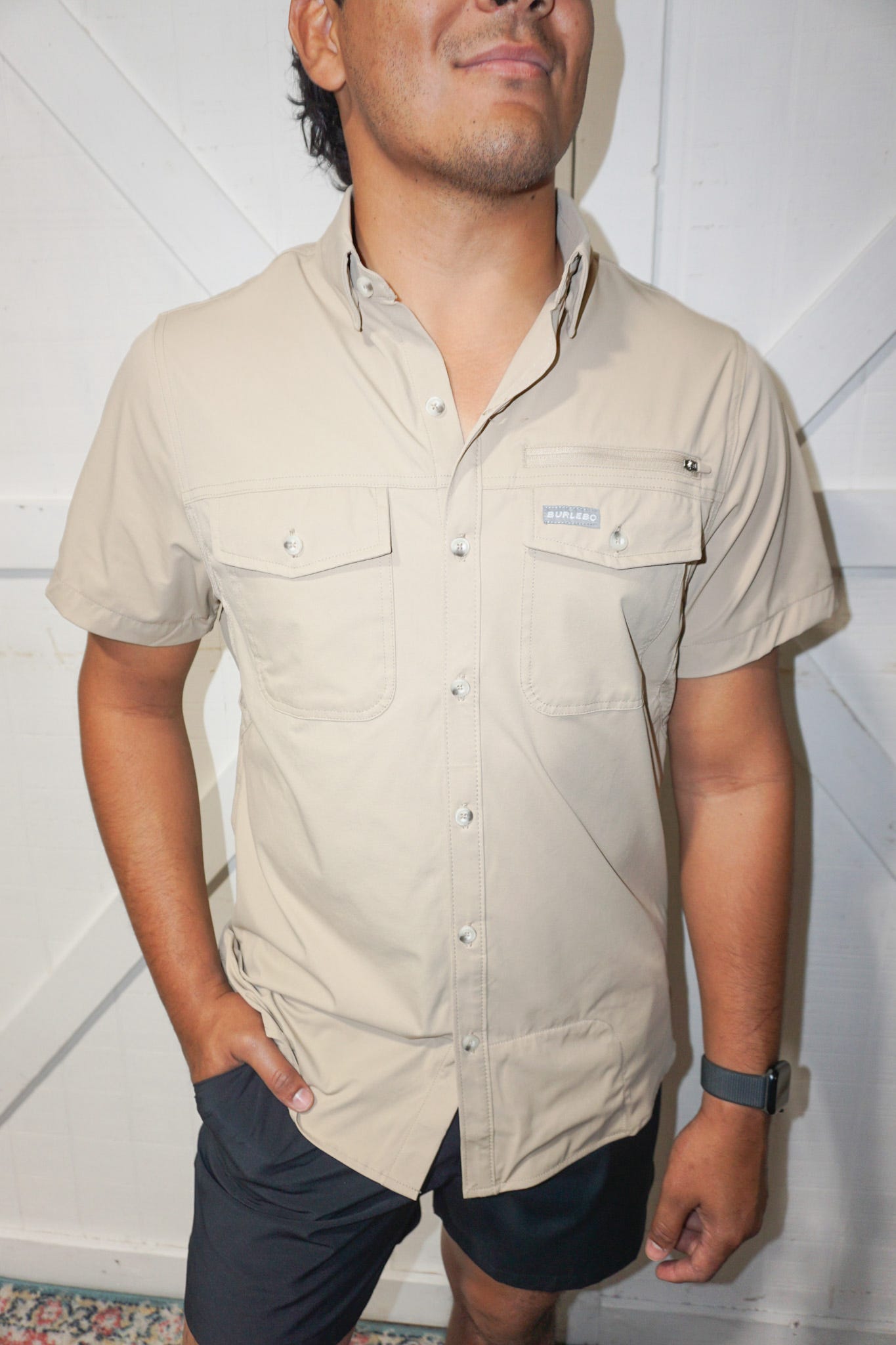 Up close photo of our tan/ khaki performance button up fishing shirt. It has short sleeves, two pockets and a zipper pocket on the front and a cape back mesh design on the back.