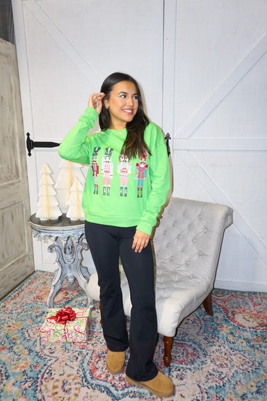 Photo of our model wearing a light green sweatshirt with four large nutcrackers on the front-all dressed differently!