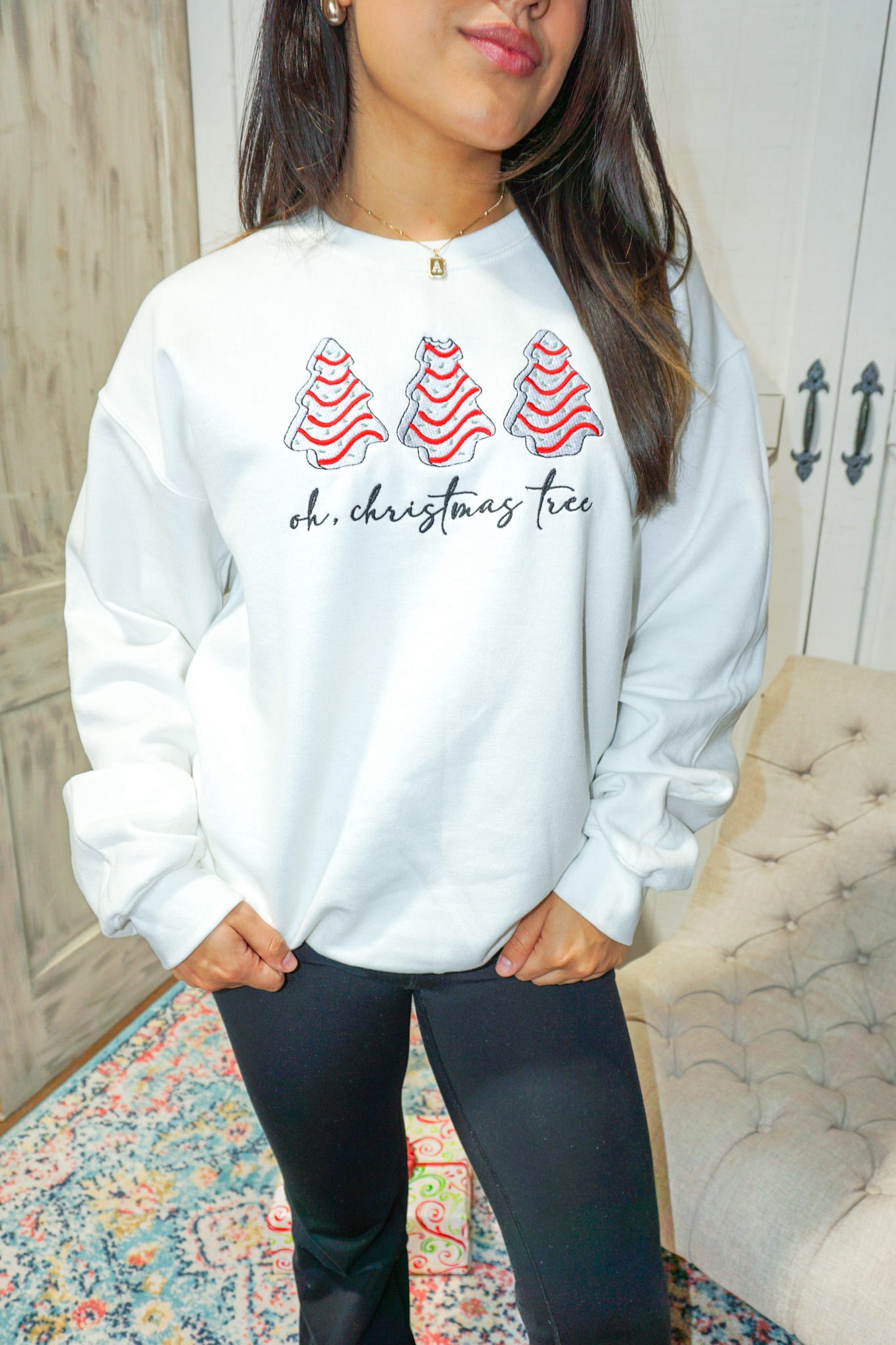 Photo of a model wearing our ash grey sweatshirt embroidered with three "Little Debbie Christmas Tree Cakes" with "oh, Christmas tree" in cursive underneath