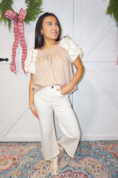 A woman modeling our light tan short sleeve blouse with cream ruffles for the sleeves.