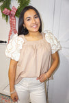 Up close photo of a woman modeling our light tan short sleeve blouse with cream ruffles for the sleeves.