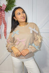 Up close photo of the tan sweatshirt with different colored striped bows sewn on all over the front