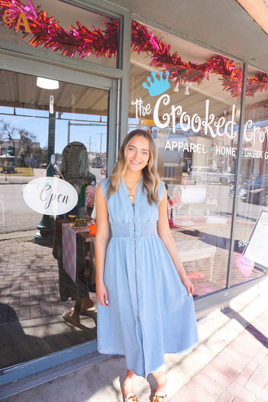 A woman modeling our light denim, sleeveless, v-neck midi dress with a zipper down the front and it has pockets too!