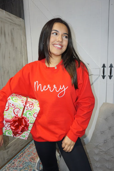 A woman modeling our red sweatshirt that's embroidered with "Merry" in white cursive on the front