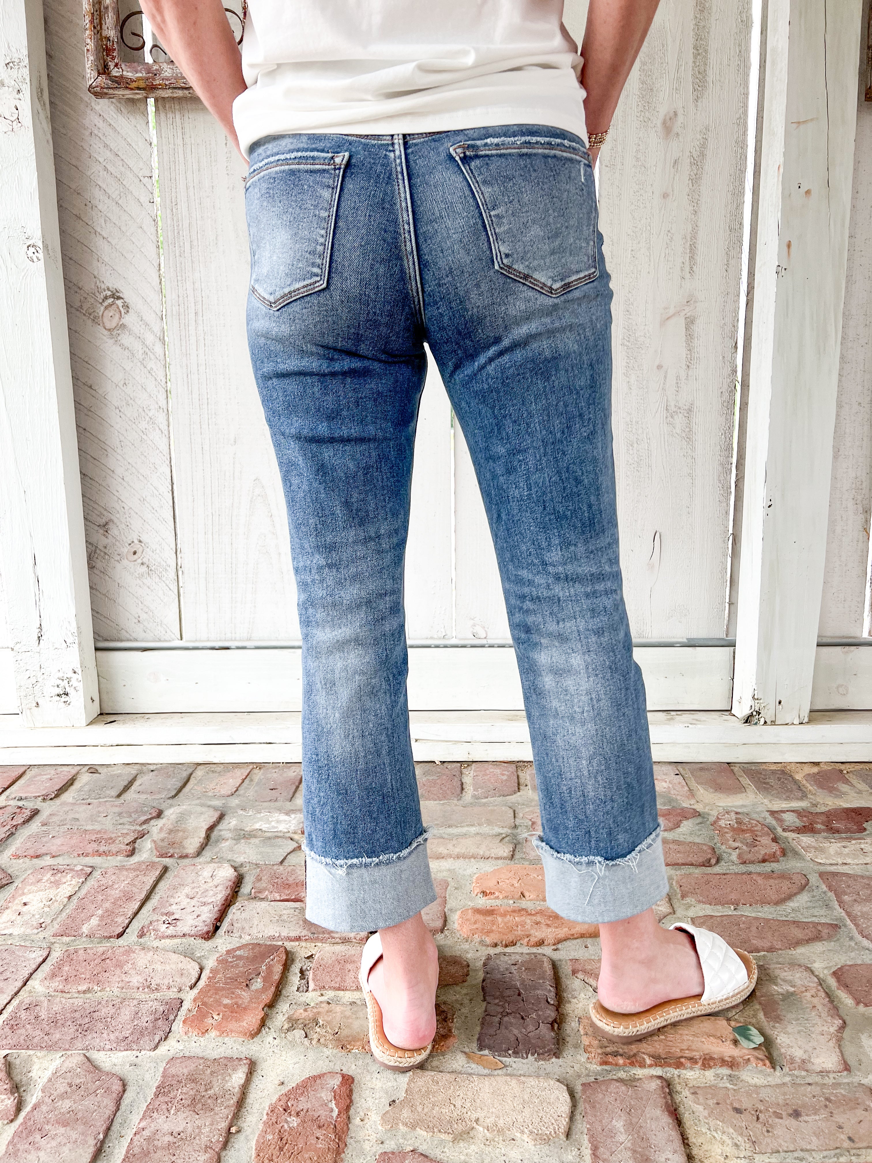 Woman modeling the back of our medium wash cropped jeans with very light distressing and a cuff at the bottom for the crop