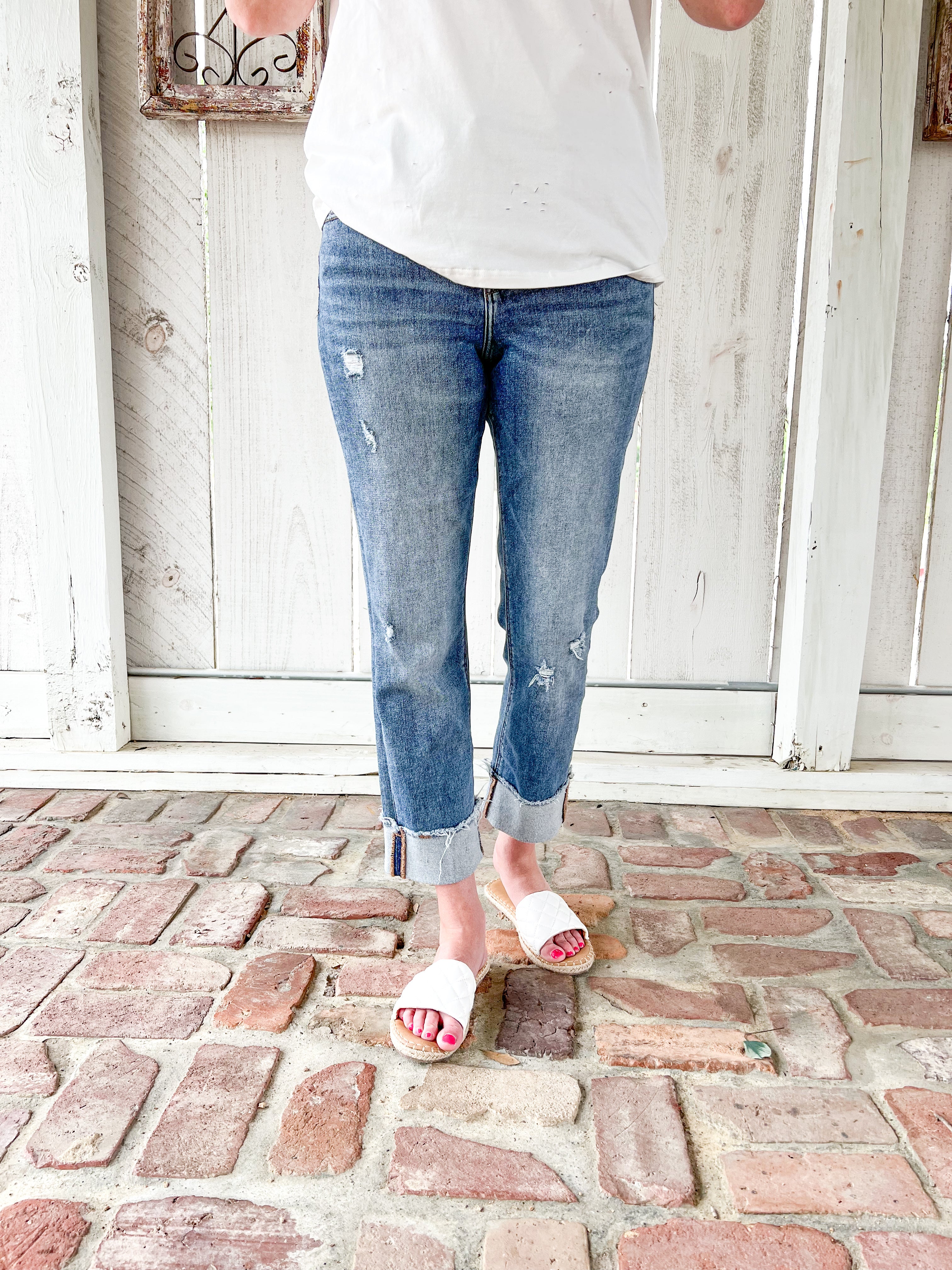 A close up photo of a woman modeling a medium wash cropped jeans with very light distressing and a cuff at the bottom for the crop