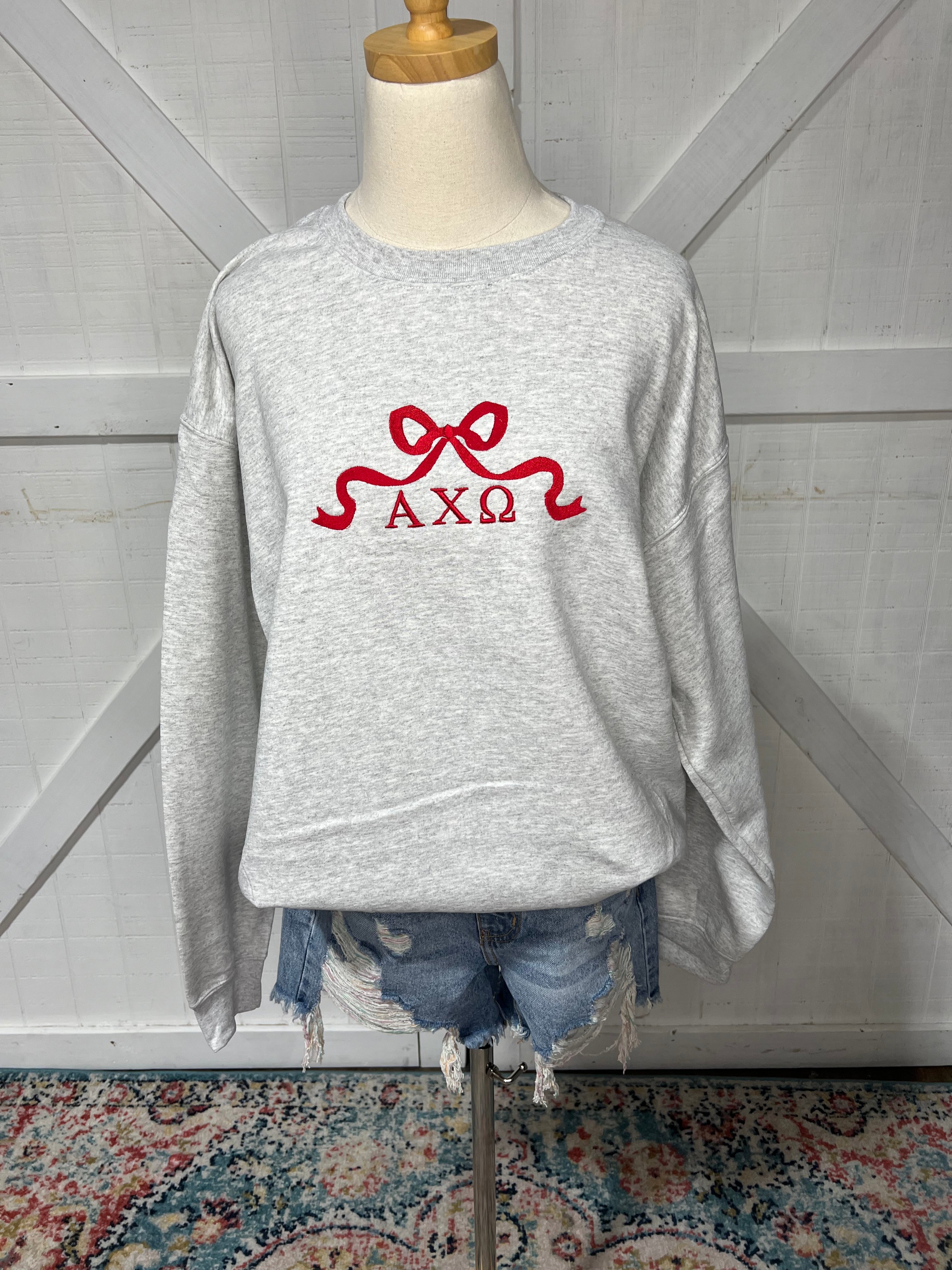 Up close photo of our AXO bow design on an Ash Grey sweatshirt