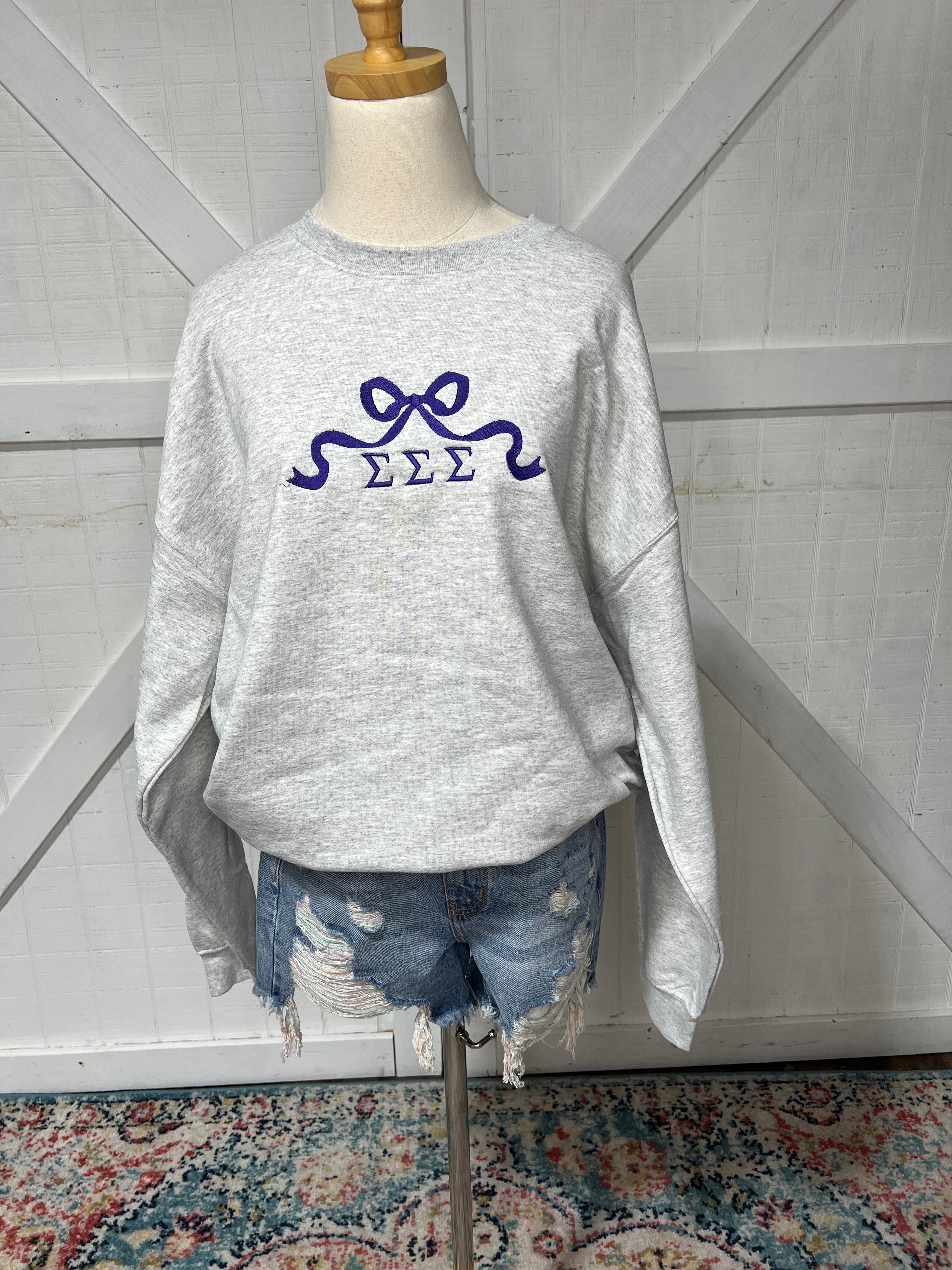 Up close photo of our Tri Sigma bow design on an Ash Grey sweatshirt