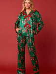 A woman modeling our green pajama set featuring a playful red bow print on both the long sleeve top and matching pants. It has a red satin trim and the front ties with red satin bows.