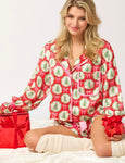 A woman modeling our red satin long sleeve and matching pajama shorts with a pattern of small Christmas trees and light pink bows all over the front and back. Pink ribbon bows tie around the wrists of the top and waist of the pj shorts.