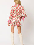 A woman modeling the back of our red satin long sleeve top and matching pajama shorts with a pattern of small Christmas trees and light pink bows all over the front and back. Pink ribbon bows tie around the wrists of the top and waist of the pj shorts.