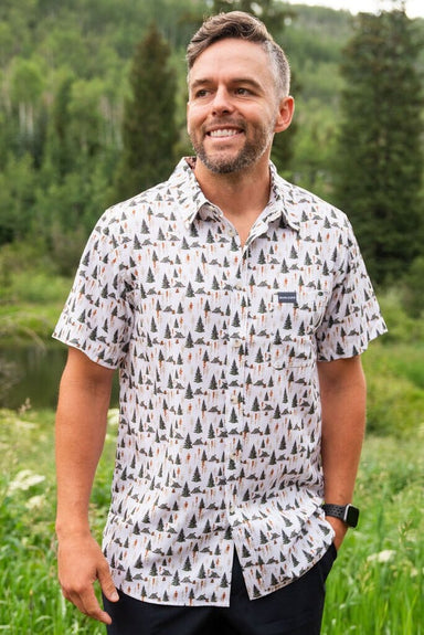 A man modeling our Campground Performance Button Up short sleeve shirt with an all-over pattern of camping tents and different trees