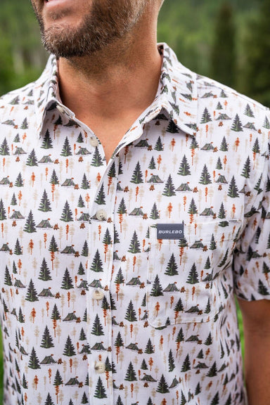 Up close photo of  our Campground Performance Button Up short sleeve shirt with an all-over pattern of camping tents and different trees.