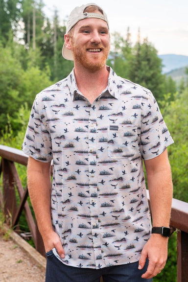 A man modeling our Duck Hunt performance Button Up short sleeve shirt with an all over pattern of ducks and marshes