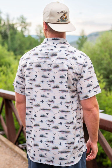 A man modeling the back of our Duck Hunt performance Button Up short sleeve shirt with an all over pattern of ducks and marshes