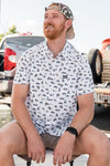 A man modeling our Houston performance button up shirt with a pattern of different symbols representing Texas all over the shirt like the Astrodome, cowboy hat, bronc rider, a guitar and the Texas flag