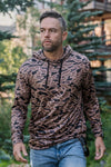 A man modeling our gauge camo performance hoodie that is a quick-dry, moisture wicking, and has UPF 50 protection. Featuring anti-microbial technology, it keeps you fresh and odor-free